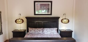 Une chambre à coucher avec une tête de lit en bois foncé, une couvre-lit à motifs floraux et deux tables de chevet surmontées de lampes rondes.