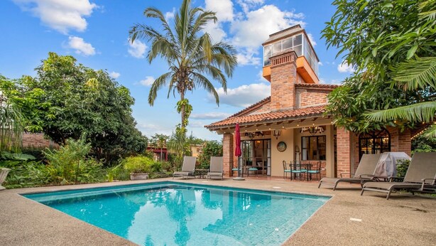 A poolside area with a clear blue pool, a brick building with a red awning, and lounge chairs.