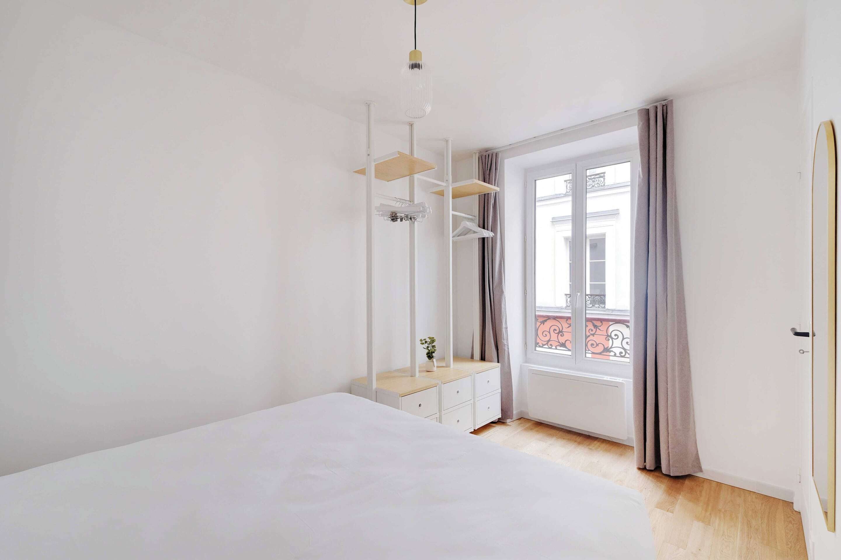 Une chambre à coucher avec un lit, une commode, un miroir et une fenêtre avec des rideaux.