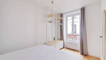 Ein Schlafzimmer mit einem Bett, einem Schminktisch, einem Spiegel und einem Fenster mit Vorhängen.