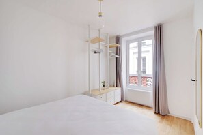 Een slaapkamer met een bed, een dressoir, een spiegel en een raam met gordijnen.