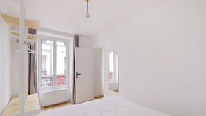 A bedroom with a bed, a wardrobe, a door leading to a balcony, and a hanging light fixture. - Charming Apartment 1br/3p - Oberkampf (Paris)
