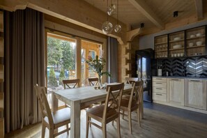 A wooden dining area with a table and chairs, a kitchen with a black refrigerator, and a view of trees outside.