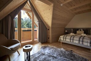 Ein Schlafzimmer mit schrägen Wänden, einem Bett mit karierter Decke, einem Sessel, einem kleinen runden Tisch und einem Fellteppich.