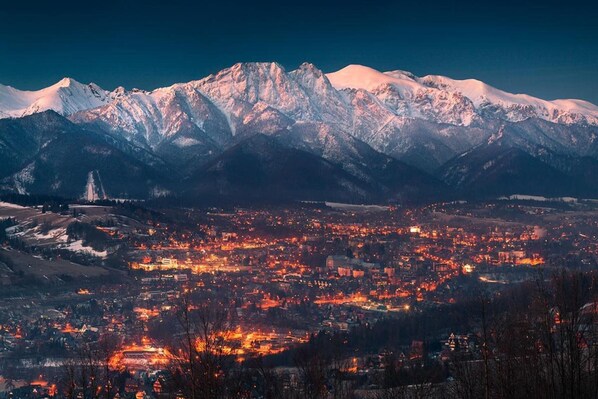 A mountainous landscape with a town in the foreground and snow-capped peaks in the background.