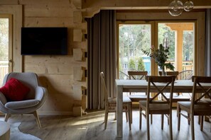 Ein Holzinterieur mit Esstisch, Stühlen, einem an der Wand montierten Fernseher und einem Fenster mit Blick auf Bäume.