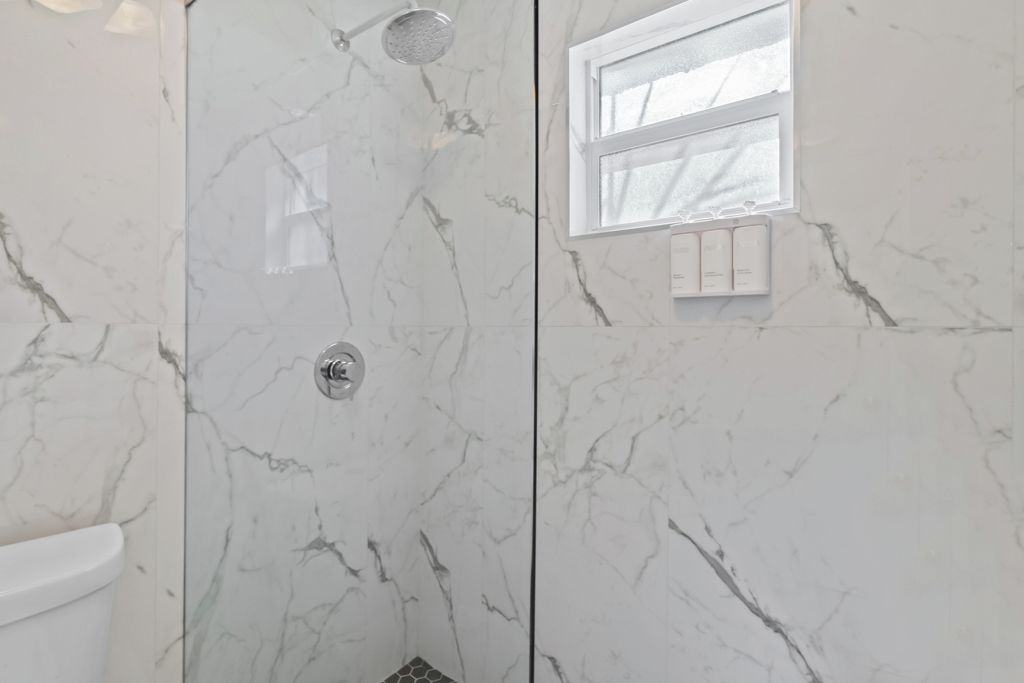 A bathroom with a shower, a toilet, and a window.