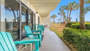 Een overdekt terras met turquoise stoelen, een glazen deuropening en uitzicht op palmbomen en de oceaan.