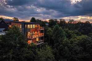 A multi-story building with balconies, surrounded by dense forest. - Amazing 5BD Pool Lodge | Theater + Hot Tub + Games (Sevierville)