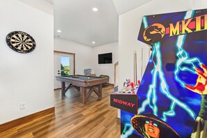 A room with a dartboard, pool table, and a poster with a character. - Amazing 5BD Pool Lodge | Theater + Hot Tub + Games (Sevierville)