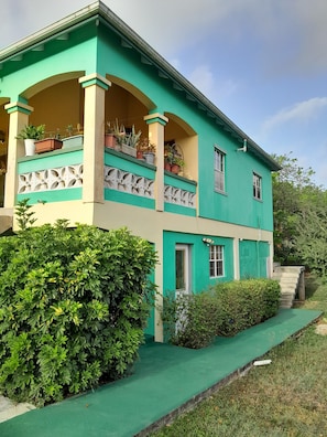 A two-story building with a balcony, a green lawn, and a staircase leading to the entrance.