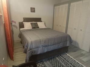 A bedroom with a bed, a bedside table, a wardrobe, and a patterned rug.