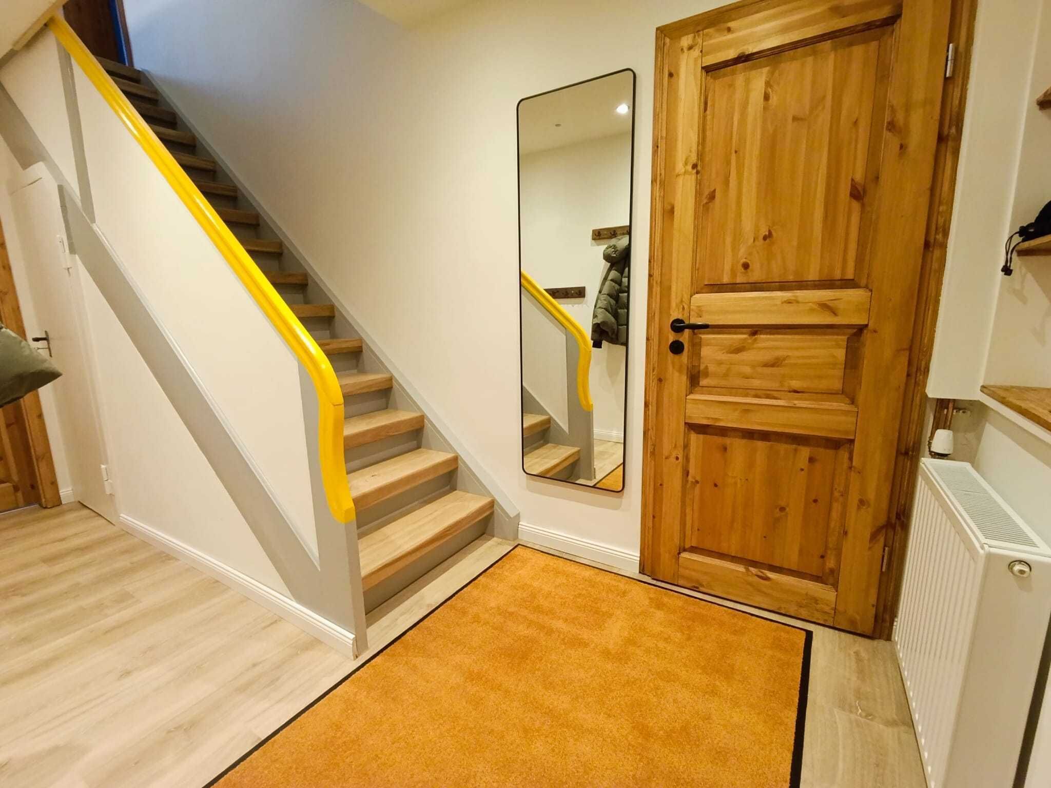 Un escalier avec une rampe jaune, une porte en bois et un miroir accroché au mur.