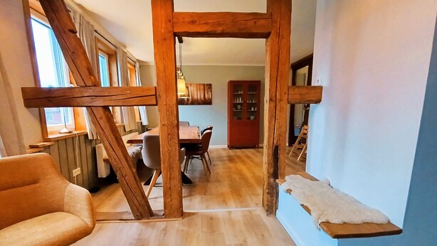 A room with a wooden staircase, a dining area with a table and chairs, and a small shelf with a white cushion. - Bergstadthaus St. Andreasberg for families & friends, child-friendly & central (Sankt Andreasberg)