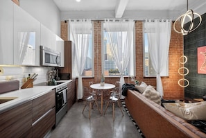 Cozinha moderna com área de refeições, parede de tijolos, cortinas brancas e vista para a cidade.