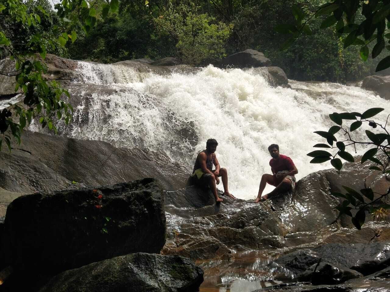 Two individuals sitting on rocks by a waterfall.