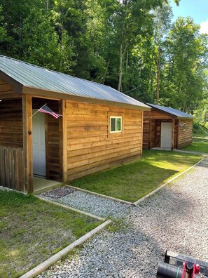 Una hilera de cabañas de madera con techos metálicos, cada una con una puerta y un pequeño ventanal.
