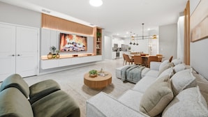 A modern living room with a large flat-screen TV, a sofa, a coffee table, and a dining area with chairs. - 7BR house sleeps 18 with private pool (Clermont)
