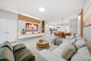 Ett modernt vardagsrum med en stor TV med platt skärm, en soffa, ett soffbord och en matplats med stolar.