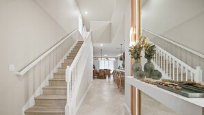 A spacious hallway with a wooden staircase and a dining area in the background. - 7BR house sleeps 18 with private pool (Clermont)