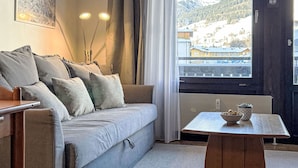 Una sala de estar acogedora con un sofá gris, una mesita de madera y vistas a un paisaje nevado a través de un ventanal grande.