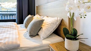 Una cama bien hecha con almohadas, una orquídea en maceta y un aplique de pared.