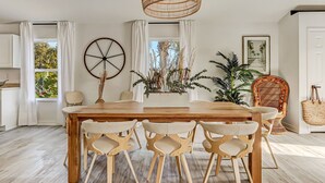 Un comedor con una mesa y sillas de madera, una lámpara colgante y un ventanal con cortinas.