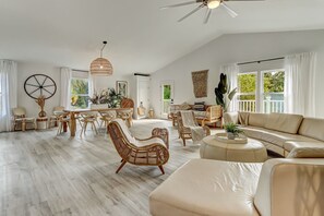 A spacious living room with a large sofa, a dining area with a table and chairs, and a ceiling fan. - Coastal Cabana/Private Pool/Walk to Beach (St. Augustine)