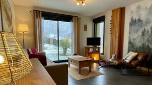 A modern living room with a wooden coffee table, a leather sofa, a TV on a wooden stand, and a large window with a view of a snowy landscape. - Gite Le 1000 Votre gîte à Loudenvielle - Comfort, nature and serenity (LOUDENVIELLE)
