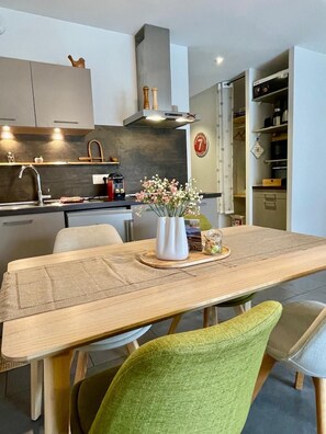 A modern kitchen with a dining area, including a wooden table, chairs, and a vase with flowers. - Gite Le 1000 Votre gîte à Loudenvielle - Comfort, nature and serenity (LOUDENVIELLE)