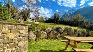 A stone wall, a picnic table, and a grassy area with a mountain backdrop. - Gite Le 1000 Votre gîte à Loudenvielle - Comfort, nature and serenity (LOUDENVIELLE)