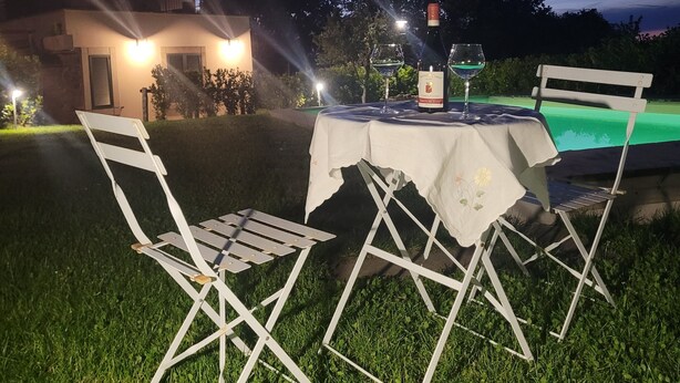 Ein Essbereich im Freien mit Tisch und Stühlen, einer Weinflasche und einem Pool im Hintergrund.