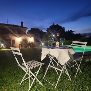 An outdoor dining area with a table and chairs, a bottle of wine, and a pool in the background. - La Sovrana dei Cimini - "Querceto" Apartment (VITERBO)