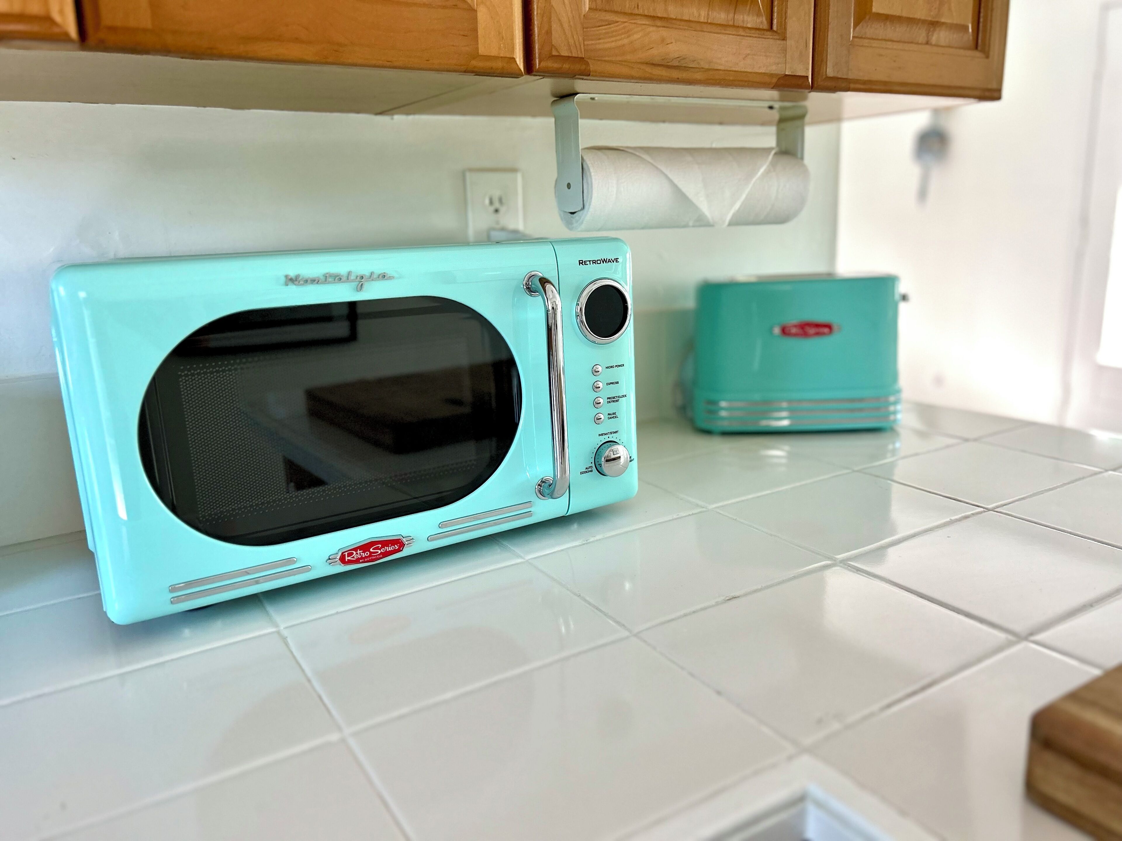 Forno de micro-ondas de estilo retrô com painel de controle e visor digital, sobre uma bancada com azulejos brancos.