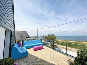 Een houten terras met blauwe en roze zitplaatsen, met uitzicht op de kust.