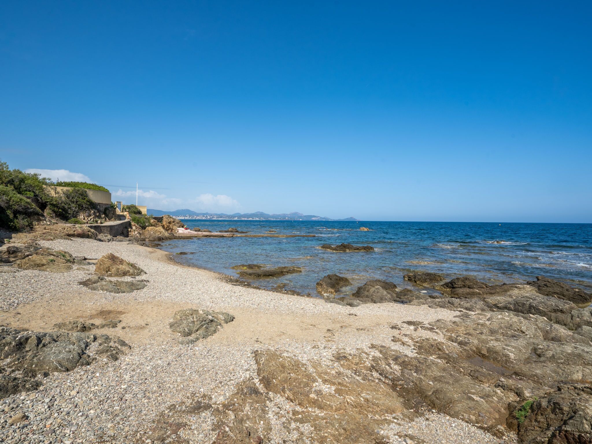 A rocky beach with clear blue water and distant mountains.