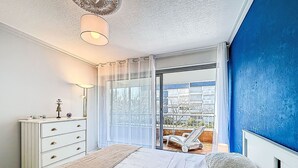 A bedroom with a bed, a dresser, a lamp, a view through a glass door, and a blue wall. - Kérabus by Interhome (Quiberon)