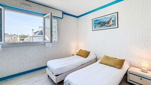 A bedroom with two beds, a window with curtains, a painting on the wall, and a bedside table with a lamp. - Kérabus by Interhome (Quiberon)