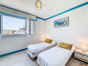 Ein Schlafzimmer mit zwei Betten, einem Fenster mit Vorhängen, einem Bild an der Wand und einem Nachttisch mit Lampe.