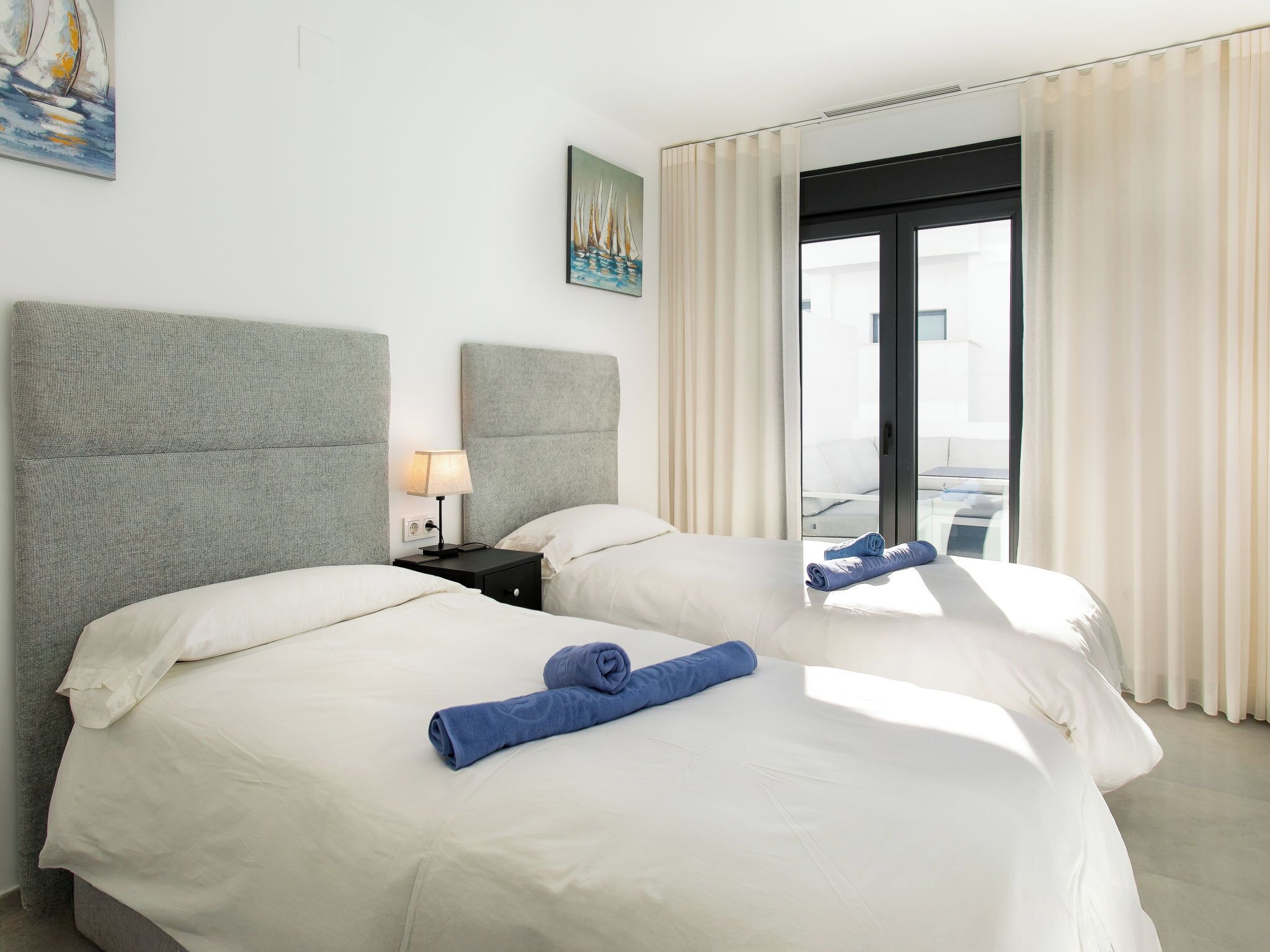 Hotelkamer met twee bedden, een nachtkastje met een lamp, een schilderij aan de muur en uitzicht door een glazen deur.
