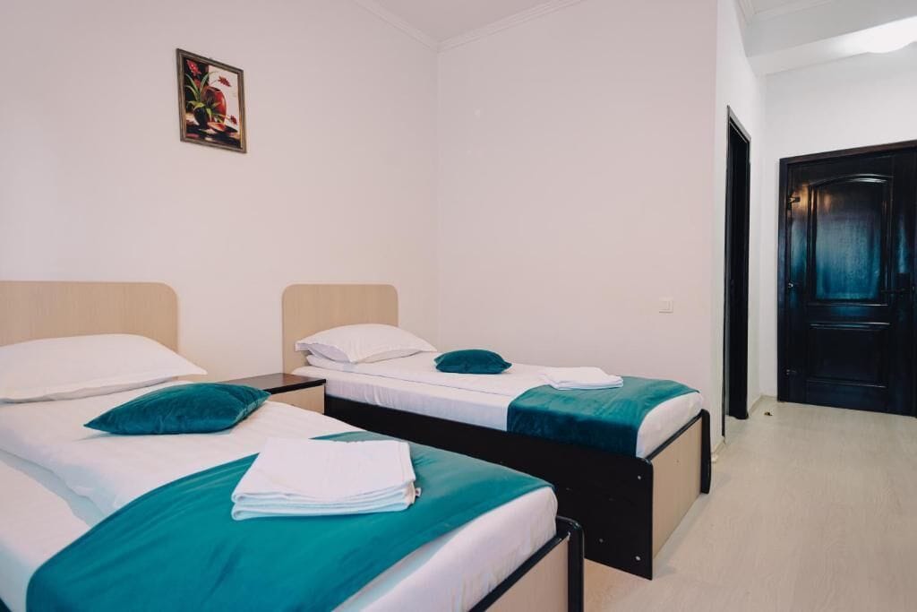 Una habitación con dos camas individuales, cada una con una colcha color aguamarina y almohadas blancas. Hay un cuadro pequeño en la pared sobre las camas.