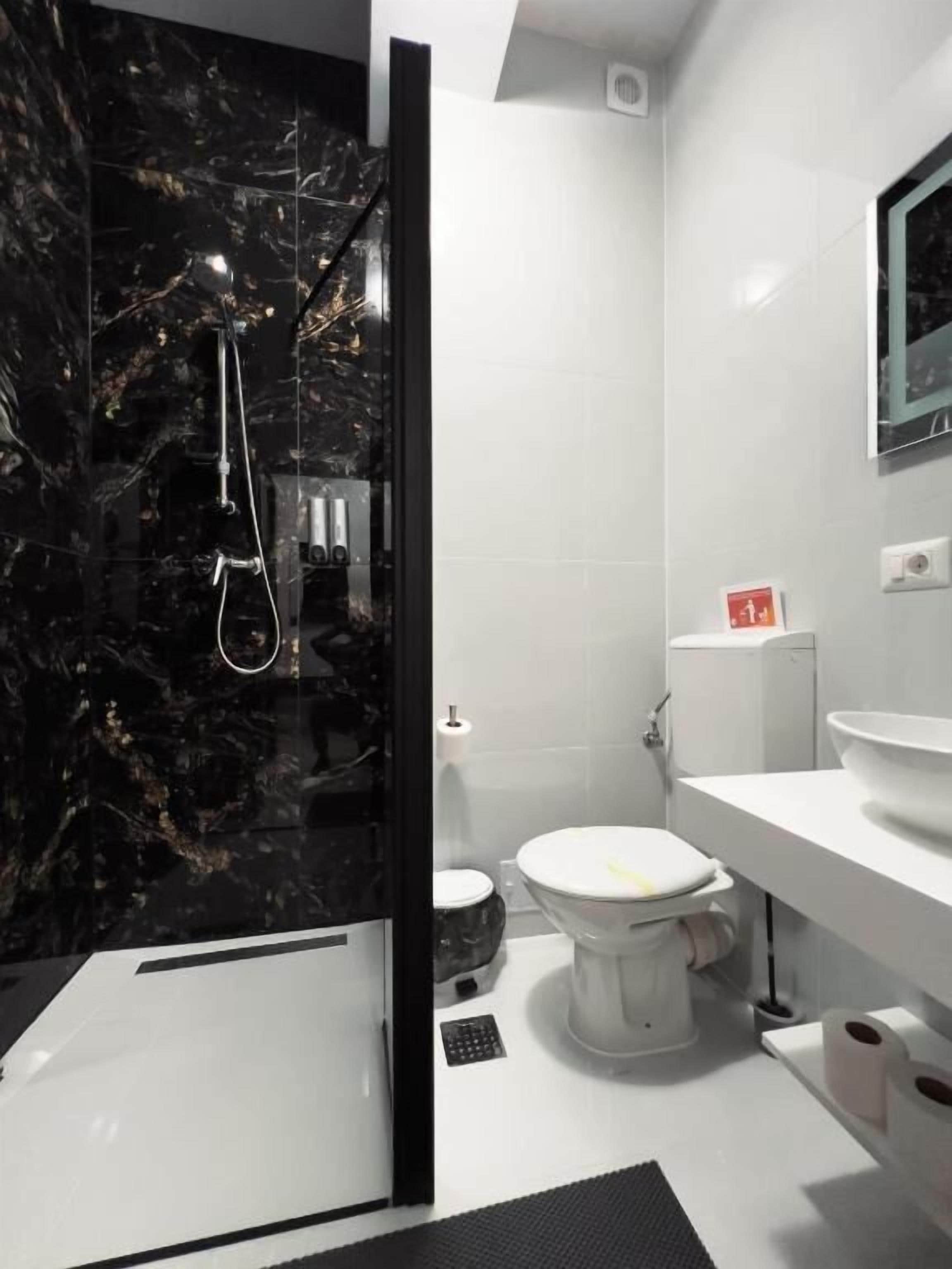Un baño moderno con cabina de ducha de mármol negro, un inodoro blanco y un lavabo blanco con un espejo arriba.
