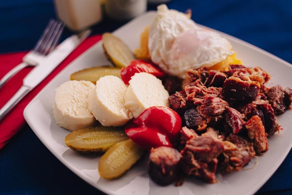 A plate of food with pickles, red peppers, and a poached egg.