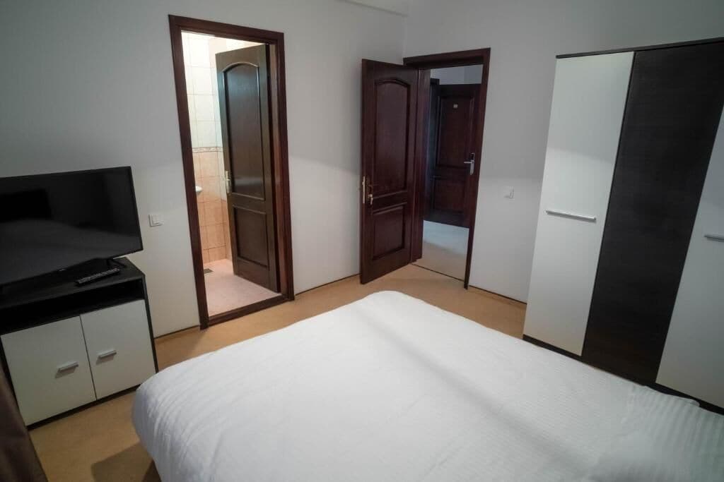 A bedroom with a bed, a TV, a wardrobe, and two doors leading to other rooms.