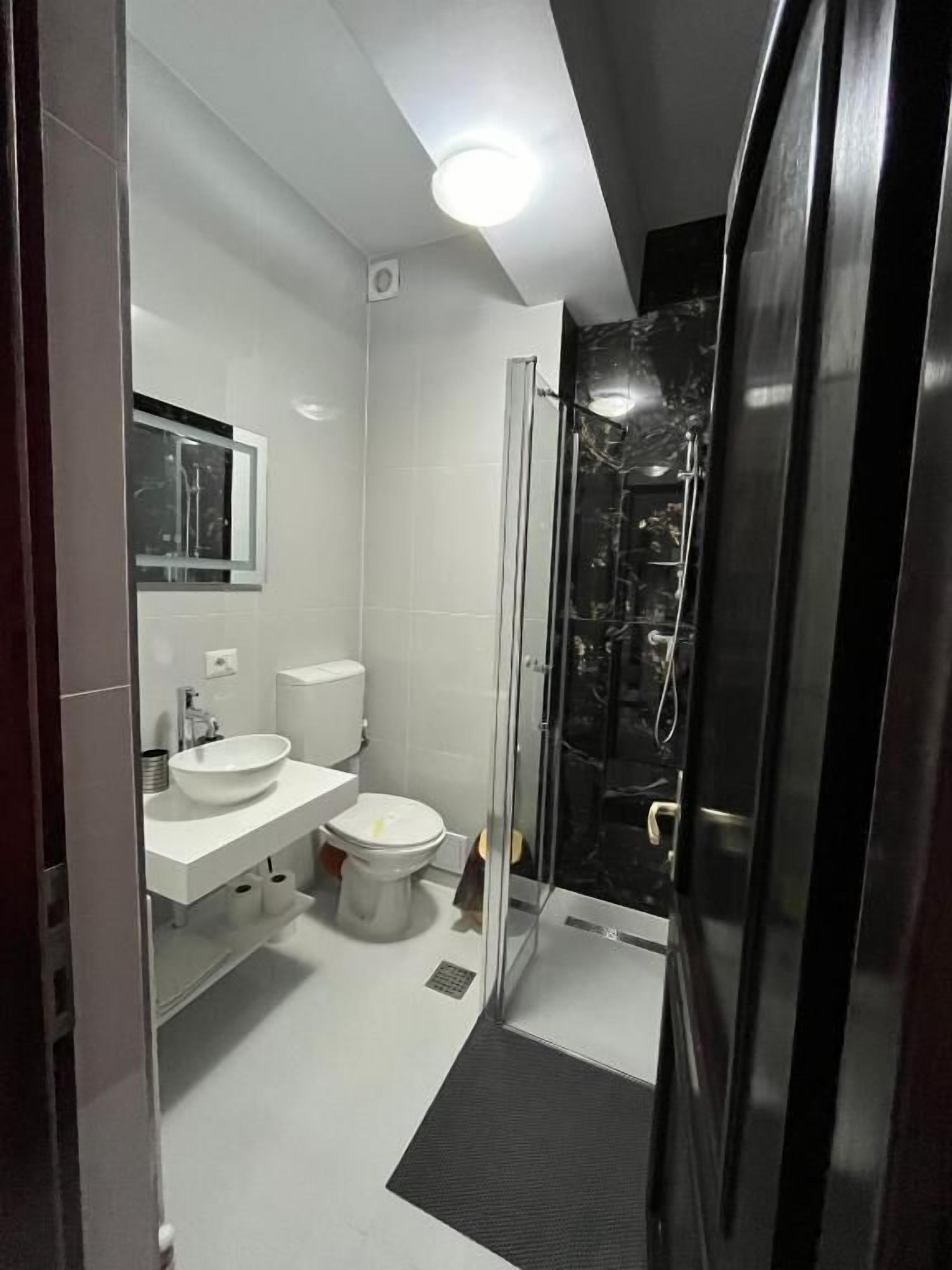 A modern bathroom with a white sink, toilet, and glass shower enclosure.