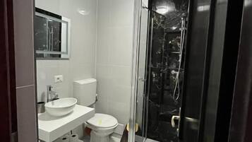 Un baño moderno con un lavamanos blanco, inodoro y cabina de ducha de vidrio.
