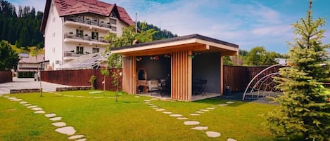 Un edificio moderno a due piani con tetto rosso, un'area salotto esterna coperta e un vialetto in pietra che conduce all'ingresso.
