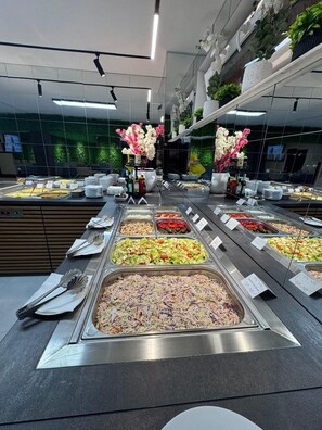 A buffet with various food options, a mirror reflecting the room, and a green wall with plants. - Chalet 173 (Gura Humorului)