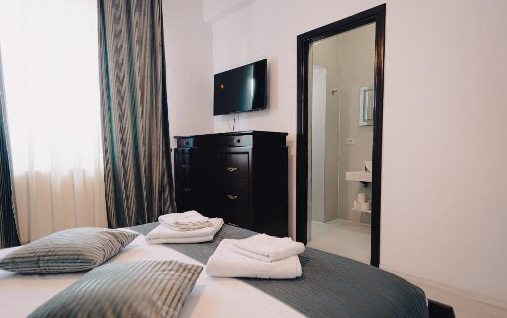 A hotel room with a bed, a flat-screen TV mounted on the wall, a wardrobe, and a mirror.