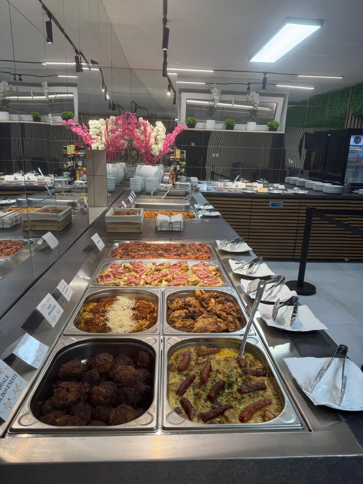 A buffet with various food options, including meats, cheeses, and salads, arranged in metal trays with labels.
